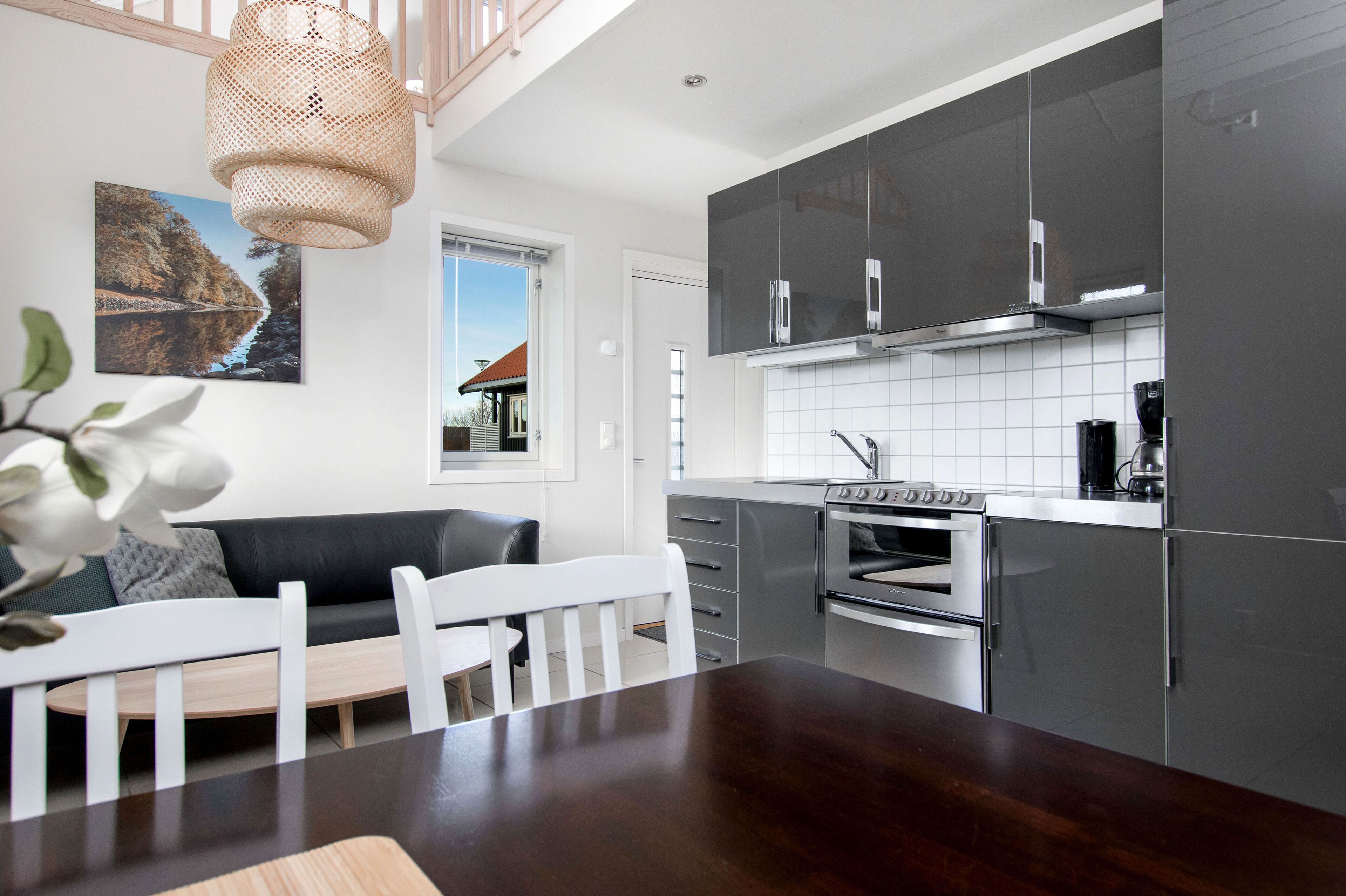 Una cocina moderna con gabinetes grises, horno empotrado y comedor con mesa de madera y sillas blancas.