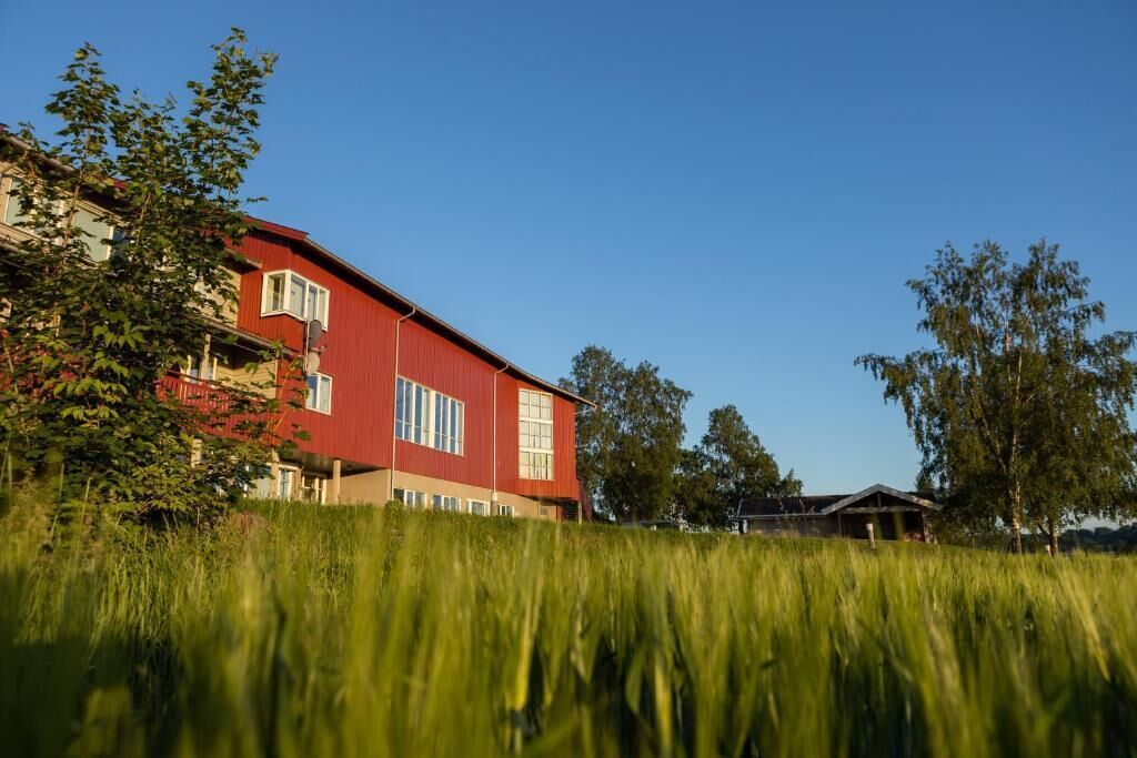 A red building with multiple windows and a flat roof, surrounded by greenery and trees.