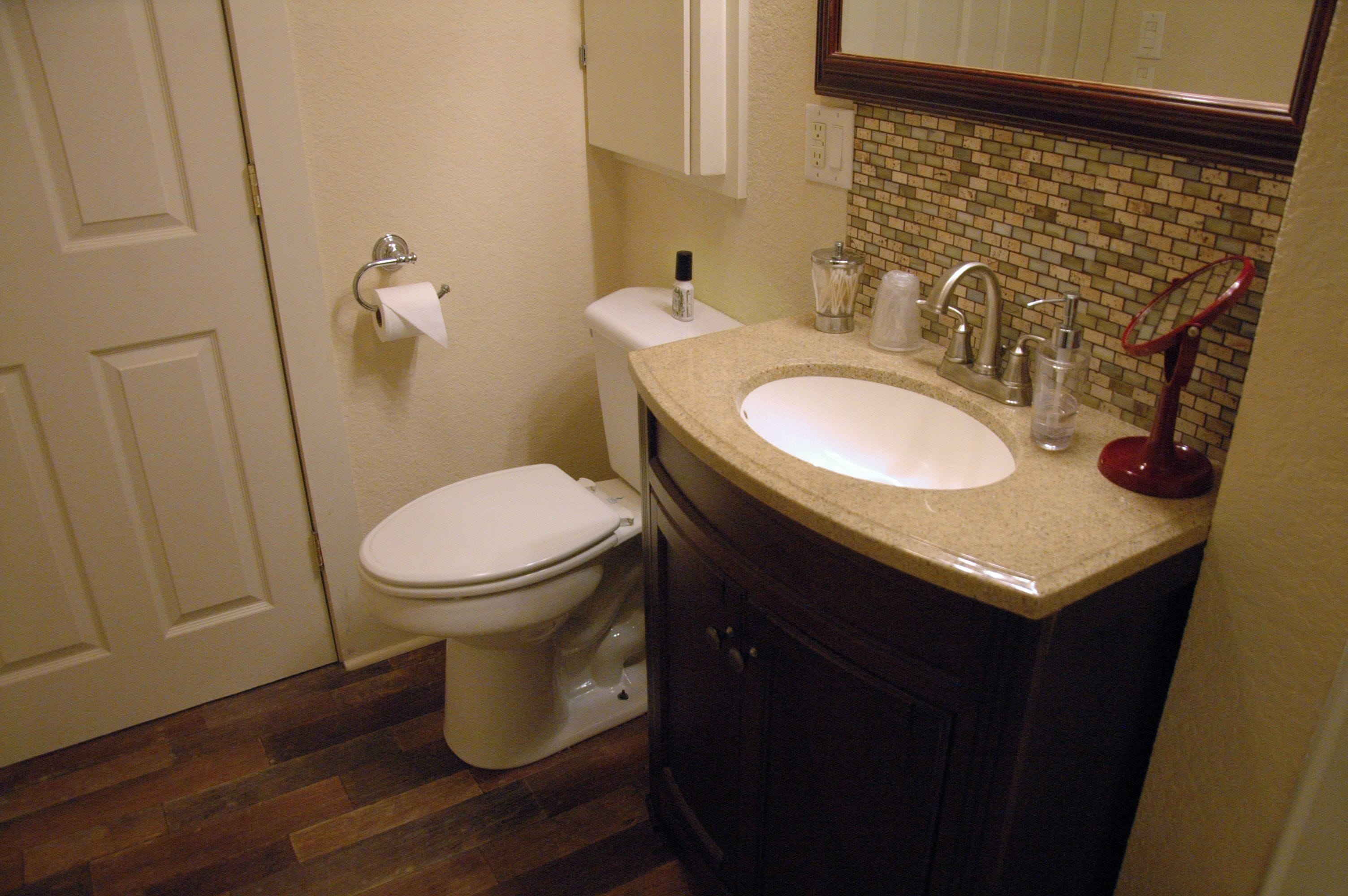 A bathroom with a toilet, sink, and mirror.