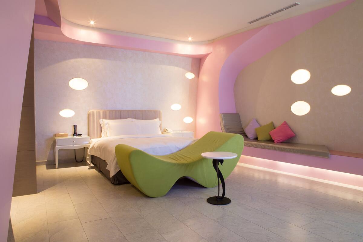 Een moderne slaapkamer met een gebogen groen bed, nachtkastjes en een klein rond tafeltje.