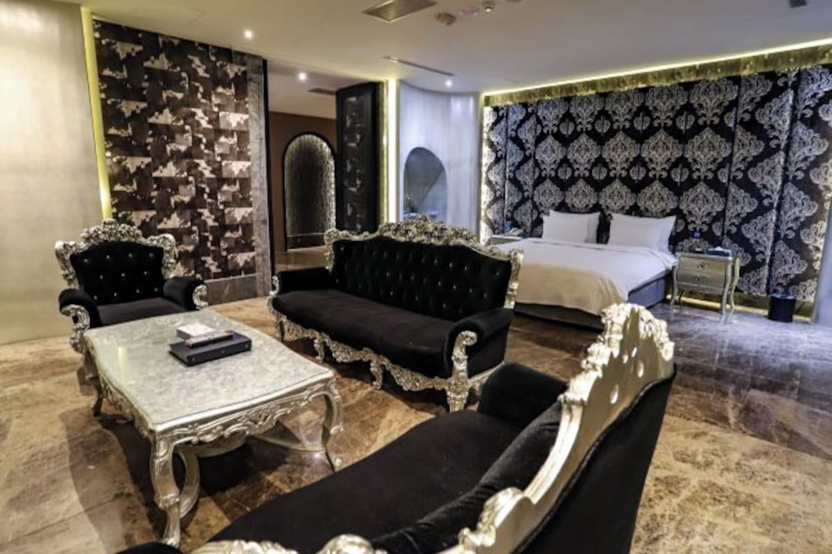 Un dormitorio lujoso con una cama grande, muebles ornamentales y un papel tapiz estampado.