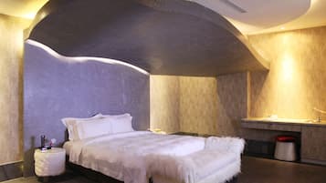 A modern bedroom with a curved ceiling, a bed with white bedding, a small bedside table, and a built-in bench.