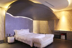 Une chambre moderne avec un plafond incurvé, un lit avec une literie blanche, une petite table de chevet et un banc intégré.