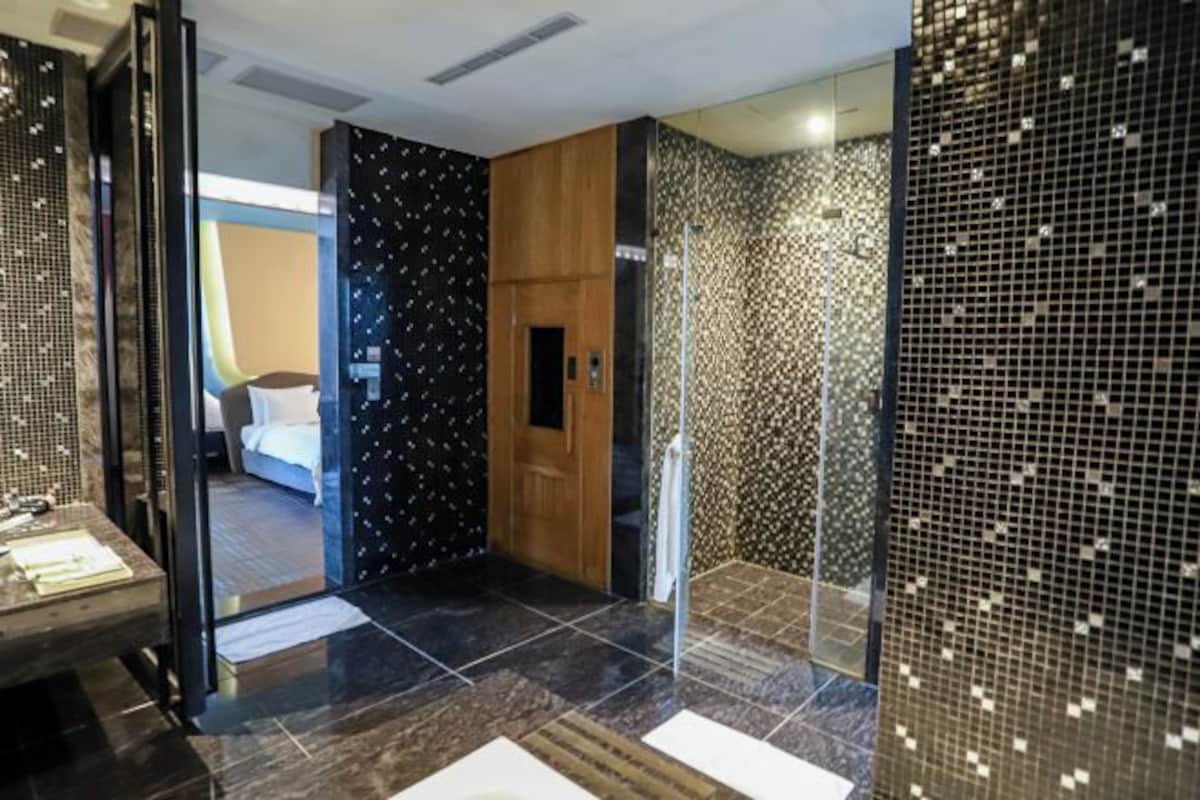 Un baño moderno con mampara de vidrio, puerta de madera y pared con diseño.