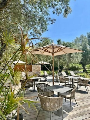 An outdoor patio area with wicker furniture, a large umbrella, and a stone wall in the background. - Hotel E Tre Stelle (Bonifacio)