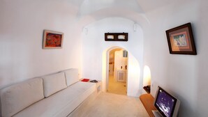 A modern, minimalist living room with a white sofa, framed artwork on the walls, and a television. - Menias Cave House (Santorini)