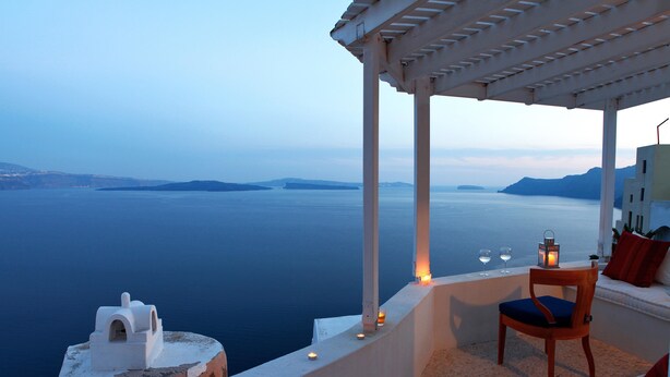 A seaside terrace with a white chair and a small table, overlooking a calm sea and distant islands. - Menias Cave House (Santorini)