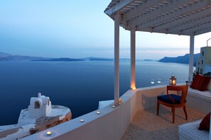 A seaside terrace with a white chair and a small table, overlooking a calm sea and distant islands. - Menias Cave House (Santorini)