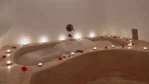 A large, oval-shaped bathtub with a curved design, surrounded by candles and red flowers. - Menias Cave House (Santorini)