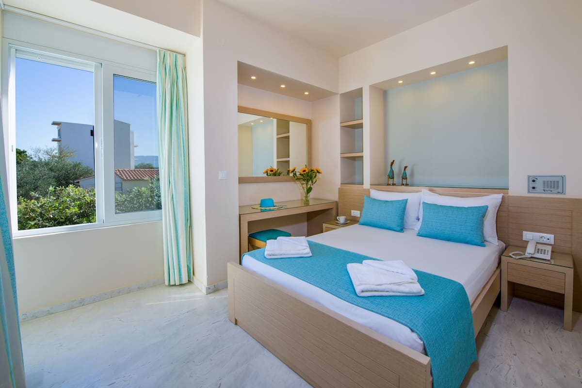 Ein modernes Hotelzimmer mit einem großen Bett, einem Schreibtisch, einem Frisiertisch und einem großen Fenster.
