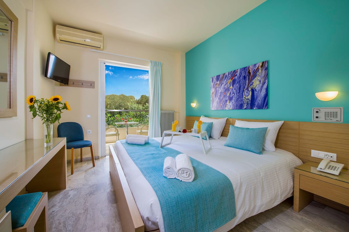 Ein Hotelzimmer mit Bett, Schreibtisch, Stuhl, Fernseher, einem Bild und Blick ins Freie.