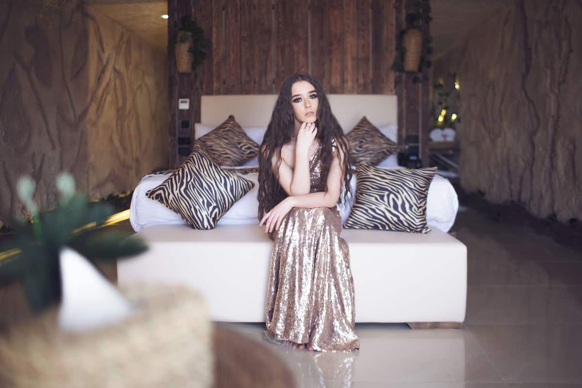 A woman sitting on a white sofa with zebra-patterned pillows in a room with wooden walls and a polished floor.