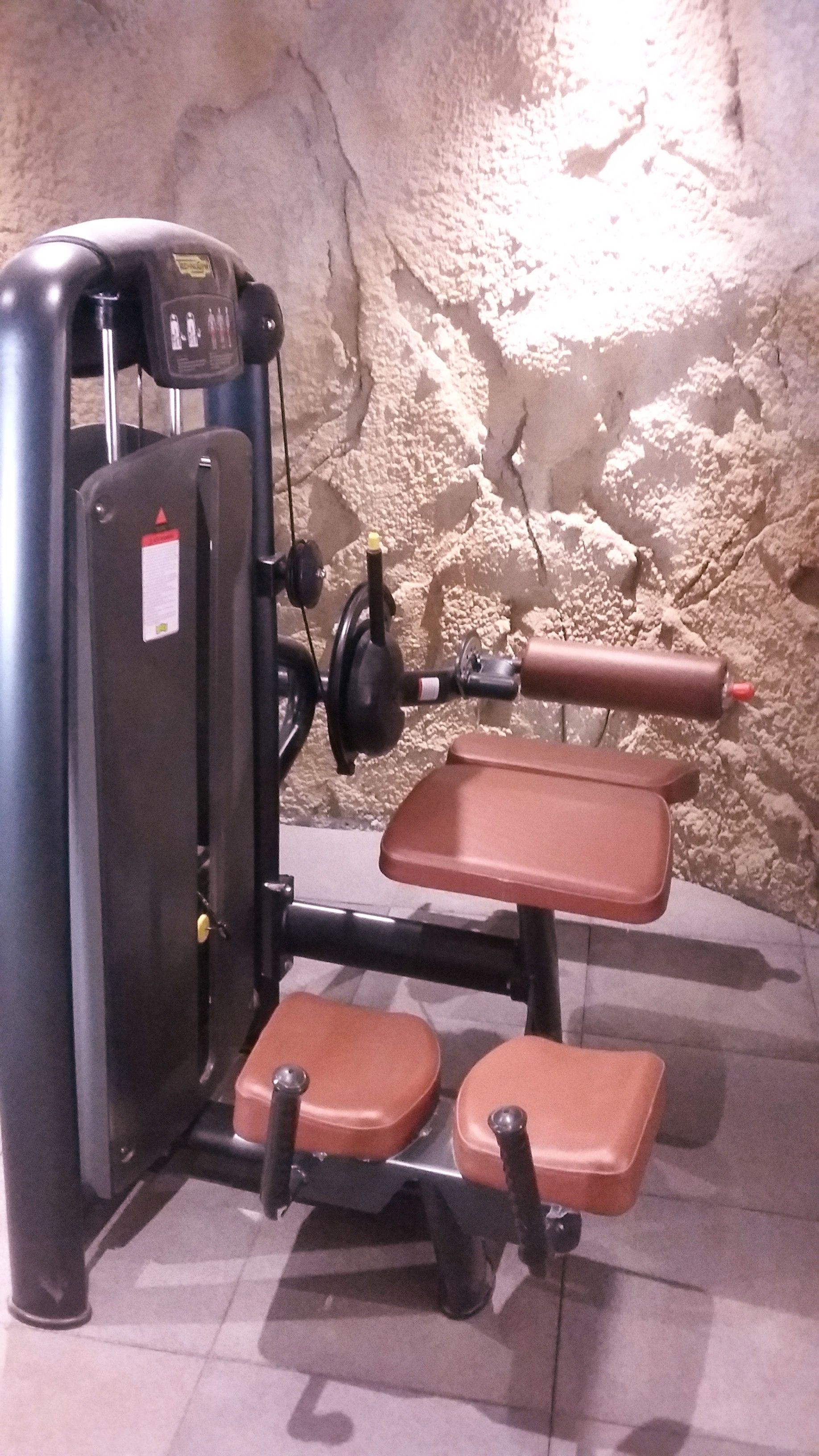Ein Fitnessraum mit Krafttrainingsgerät, Bänken und einer Wand mit strukturierter Oberfläche.