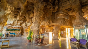 A spacious lobby with a high ceiling and natural rock formations, a reception desk, seating area, and potted plants. - Caves Beach Resort Hurghada - Adults Only - All Inclusive (Hurghada)