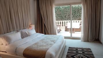 A bedroom with a large bed, a view of the outdoors, and a balcony with furniture.