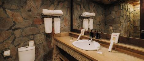 A bathroom with a stone wall, a sink, a mirror, and two towel dispensers.