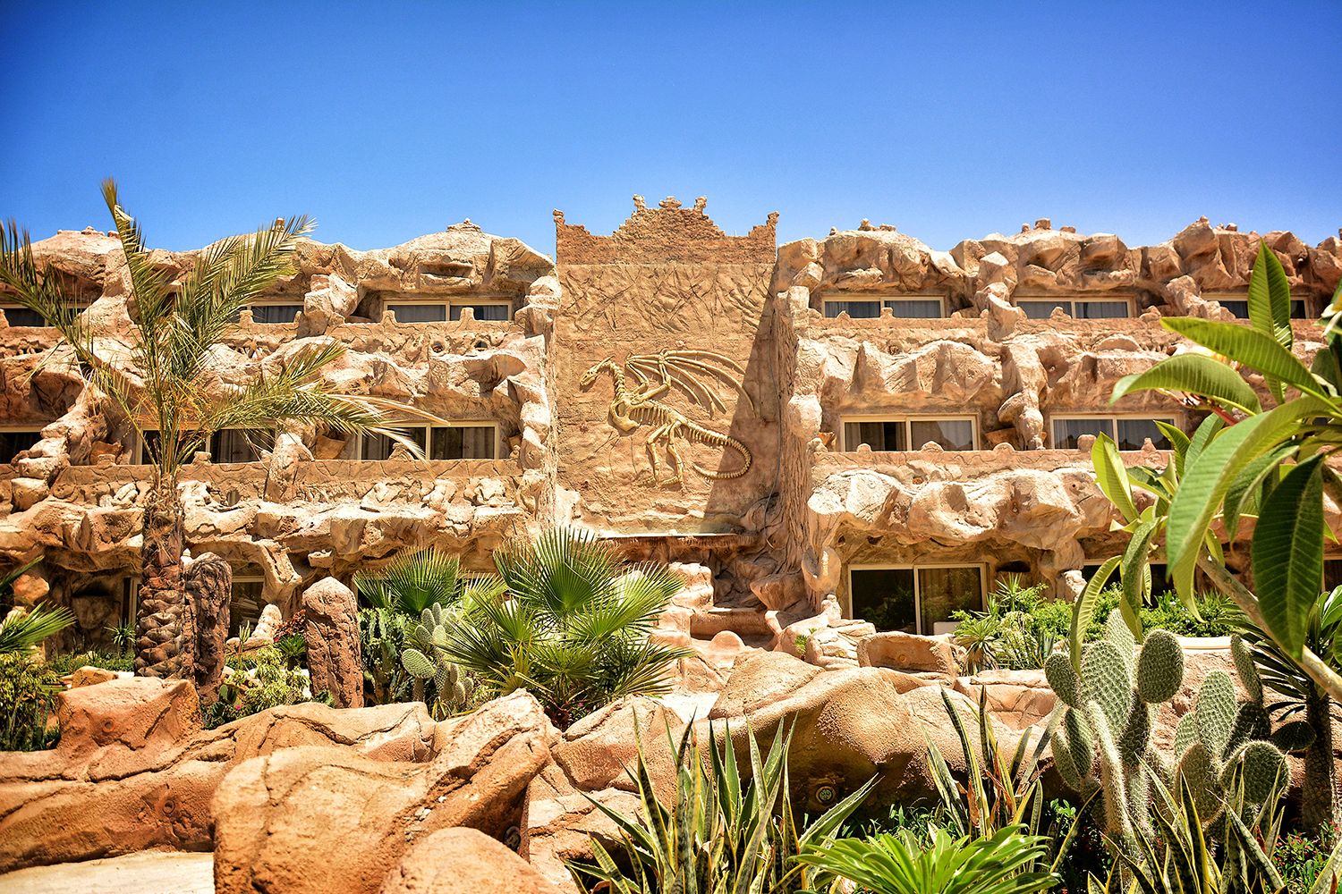 Ein Hotel mit Wüstenarchitektur, darunter Felsformationen und eine Dinosaurierskelett-Skulptur.