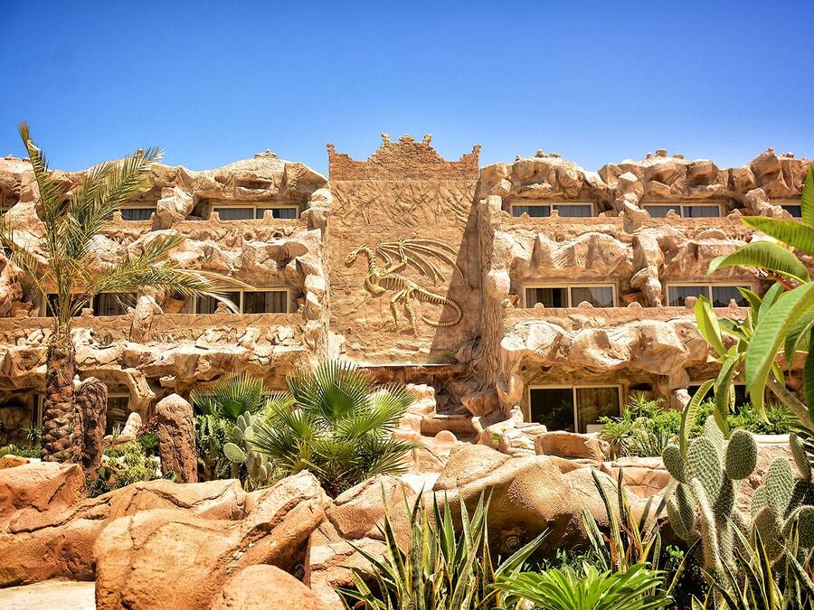 Ein Hotel mit Wüstenarchitektur, darunter Felsformationen und eine Dinosaurierskelett-Skulptur.