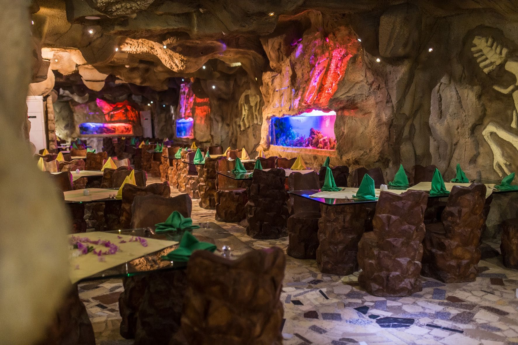 Ein Restaurant mit gedeckten Tischen auf einem Mosaikboden, umgeben von Felsformationen und prähistorischen Tierreliefs.