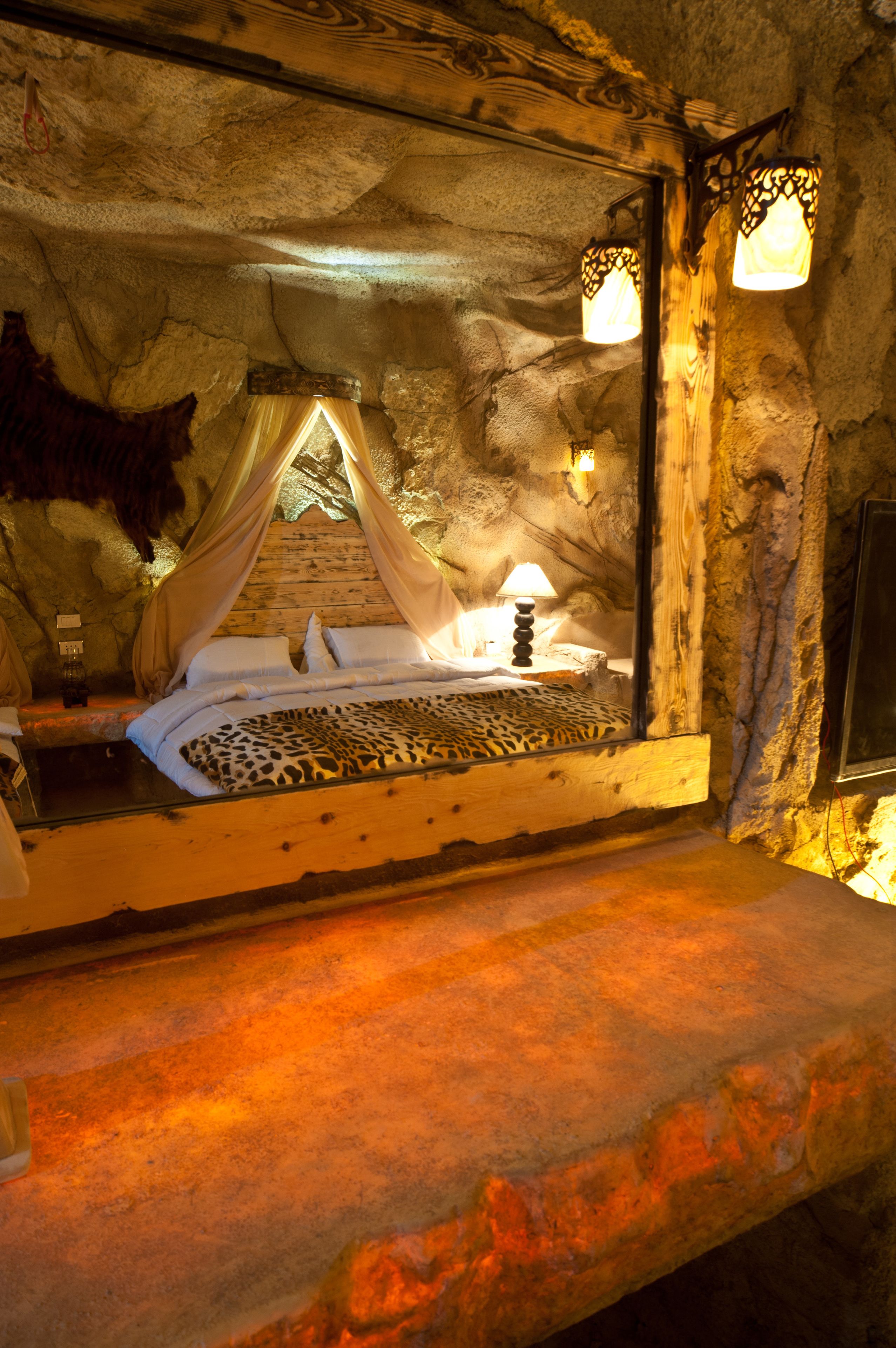 Un interior rústico de piedra con una cama que tiene dosel y una colcha de estampado de leopardo.