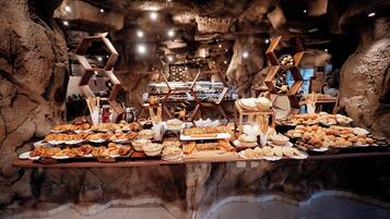 A buffet with various food items displayed on wooden stands, set against a cave-like interior with rock formations and hexagonal wooden structures.