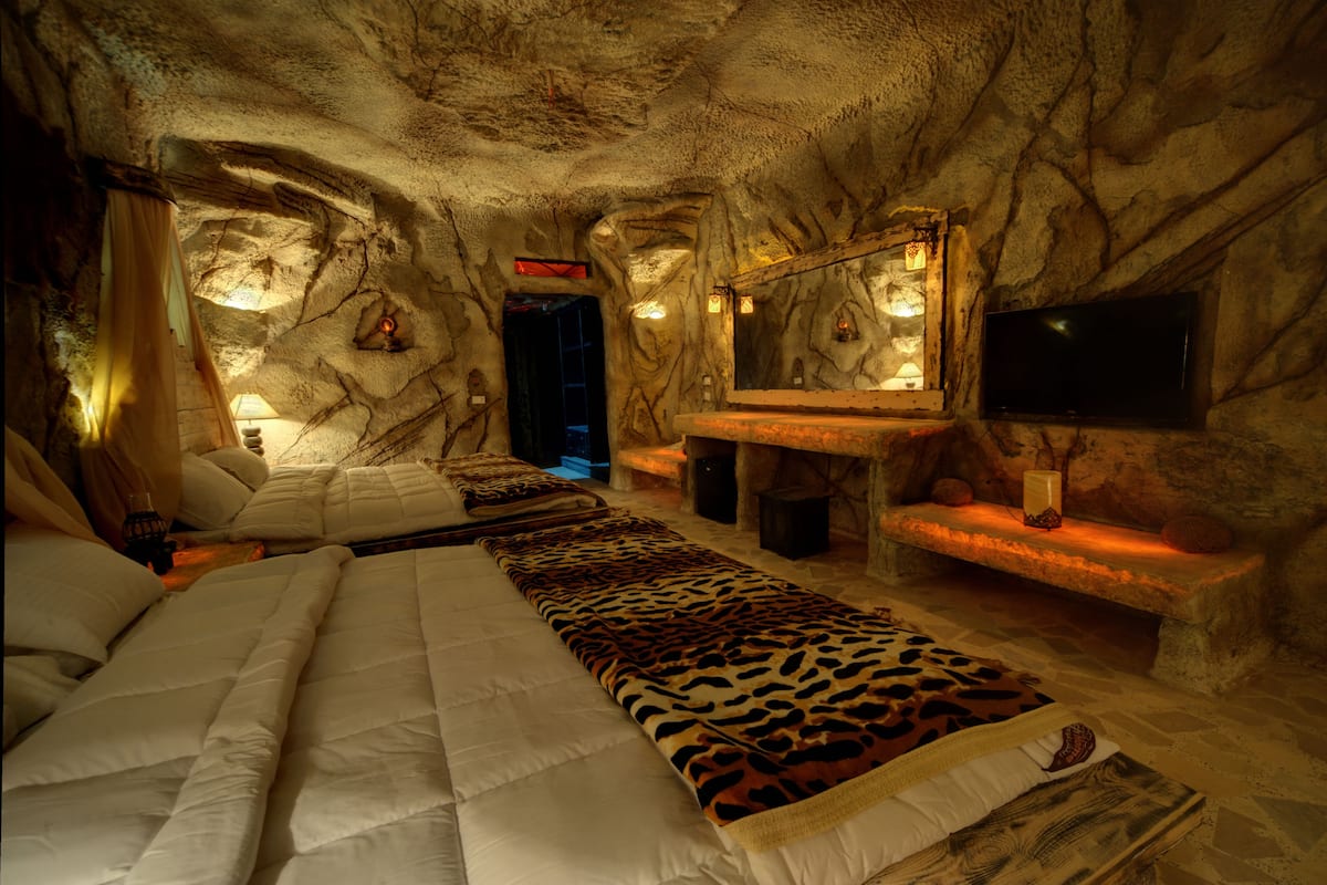 A cave-like room with a bed, a bench, a TV, and a mirror.