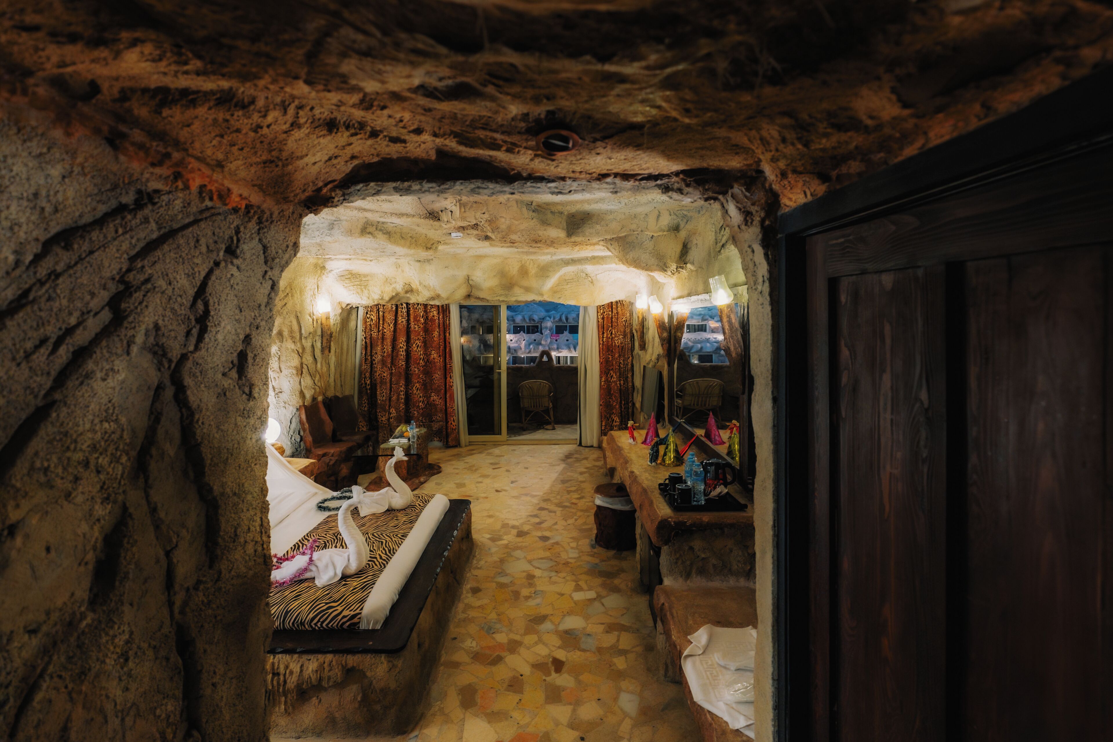 Una habitación tipo cueva con una cama, un banco de madera y una mesa con diversos objetos.