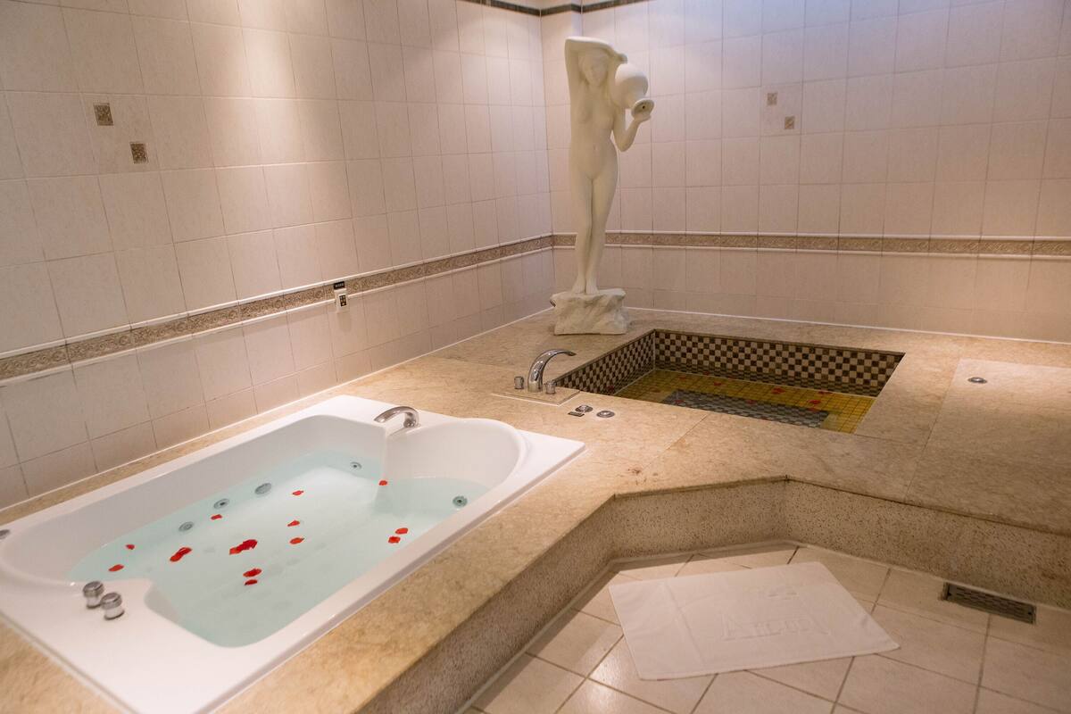 Un baño moderno con una bañera grande, un lavamanos pequeño y una estatua decorativa.