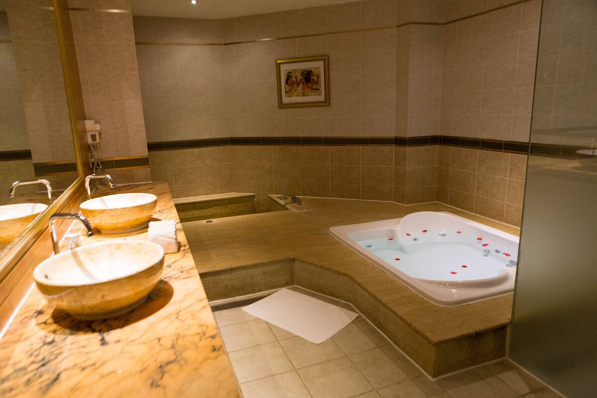 Un baño con tres lavamanos, una bañera y un espejo grande.