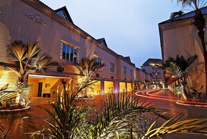 Une cour d’hôtel avec un chemin sinueux, des palmiers et une entrée bien éclairée.
