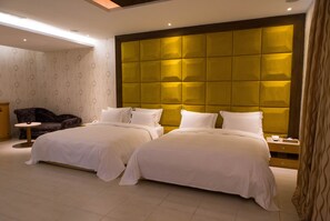 Une chambre d’hôtel avec deux lits, une petite table ronde, une chaise et une grande tête de lit éclairée.