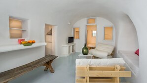 Een kleine kamer met een bed, een tafeltje, een bankje en een televisie.
