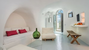 Een moderne, minimalistische woonkamer met een witte bank, rode kussens, een groene vaas en een houten bankje.