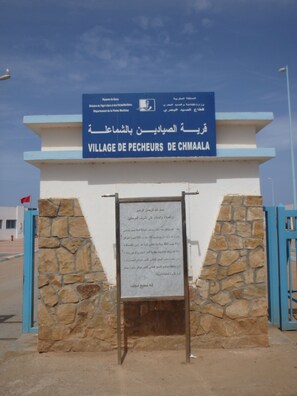 Een bordje voor het Village de Pecheurs de Chmala, met een stenen muur en blauwe poorten.