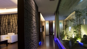 Un lobby moderno con pared de piedra, zona de estar y un espacio de vidrio con plantas.