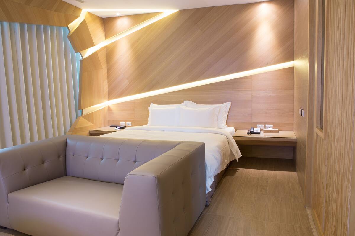 A modern bedroom with a bed, bedside tables, a sofa, and a wooden accent wall.