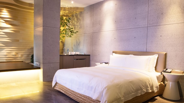 Una habitación de hotel moderna con una cama grande, una mesita de noche y un espejo fijado a la pared.