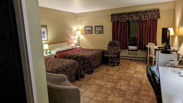 Ein Hotelzimmer mit einem Bett, zwei Stühlen, einem Schreibtisch und einem Fenster mit Vorhängen.