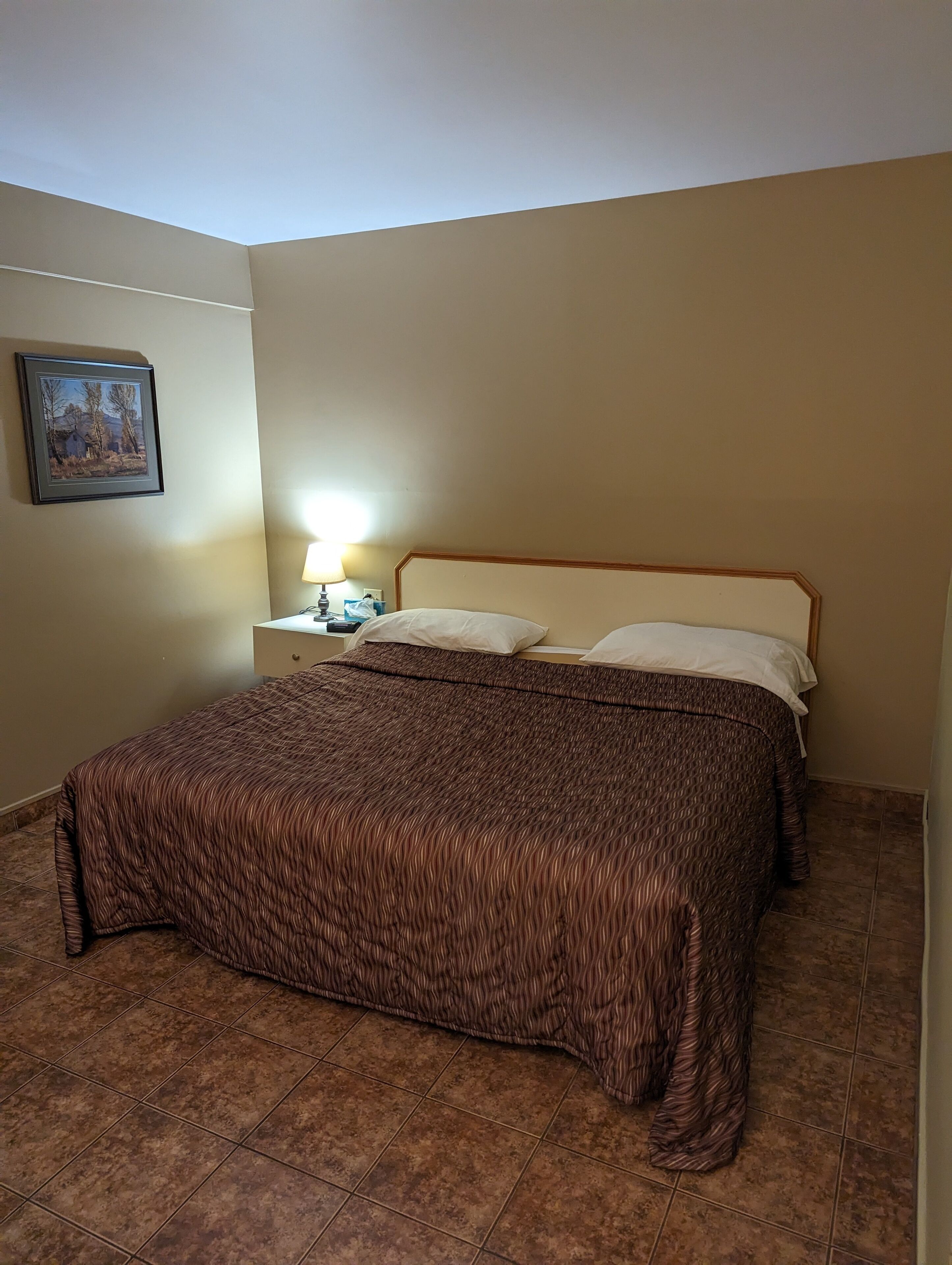 A bedroom with a bed, a nightstand, a lamp, and a framed picture on the wall.