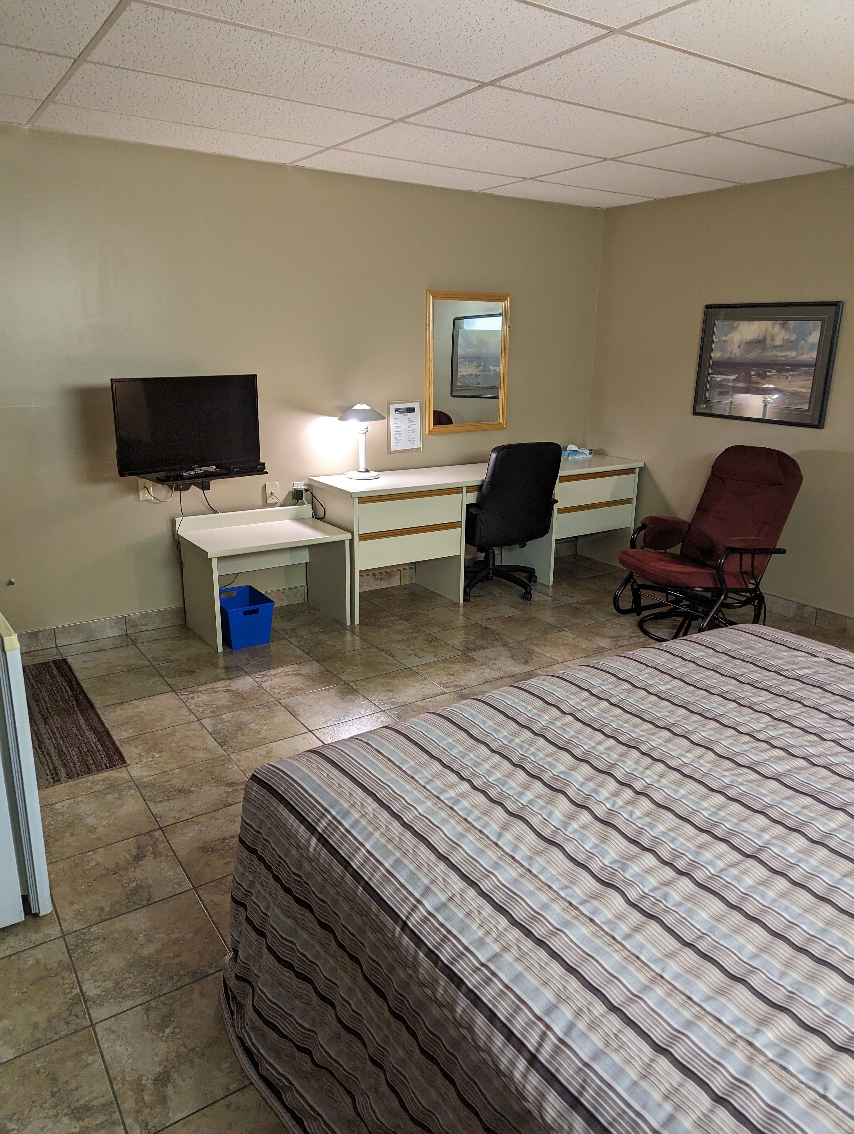 A hotel room with a bed, desk, chair, television, and a mirror.
