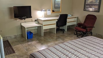 A hotel room with a bed, desk, chair, television, and a mirror.