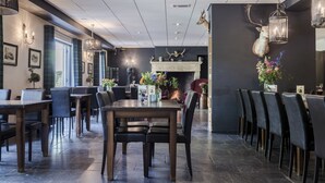 A modern dining area with a fireplace, dark walls, and a mounted deer head. Tables and chairs are arranged for dining. - Hotel De Kruishoeve (Vught)