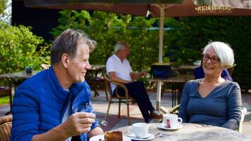 Two people sitting at an outdoor table with a cake and a cup.