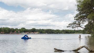 Un lago tranquilo con un bote inflable azul y una persona en una tabla de remo.