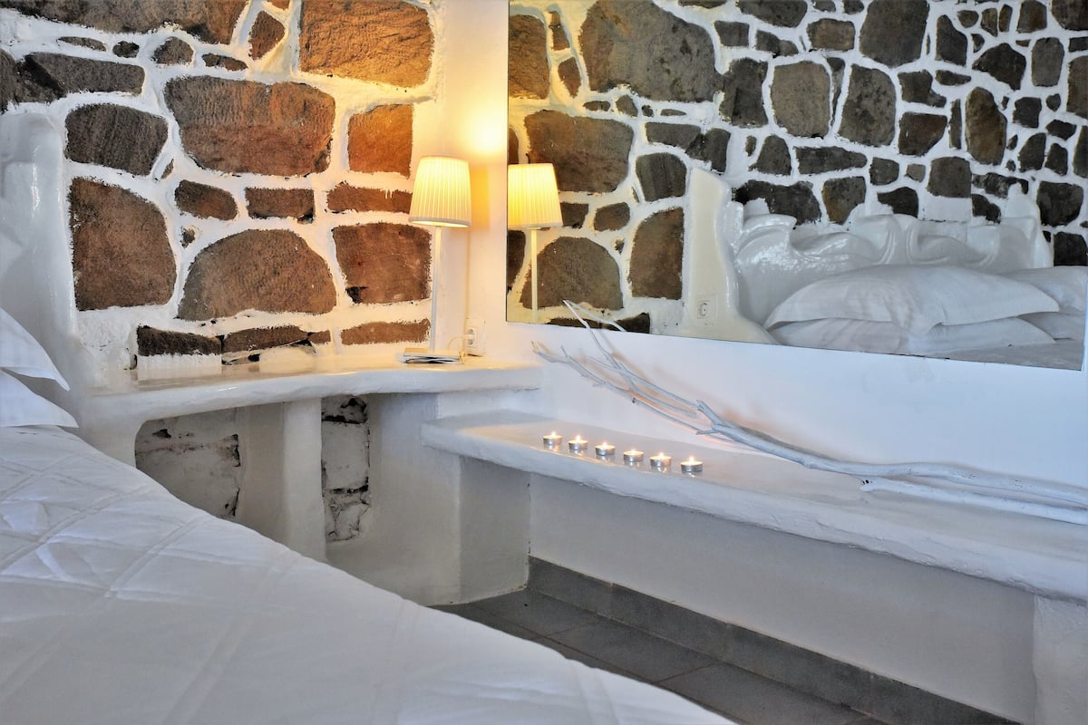 A stone-walled bathroom with a bathtub, two wall-mounted lamps, and a bed with white linens.