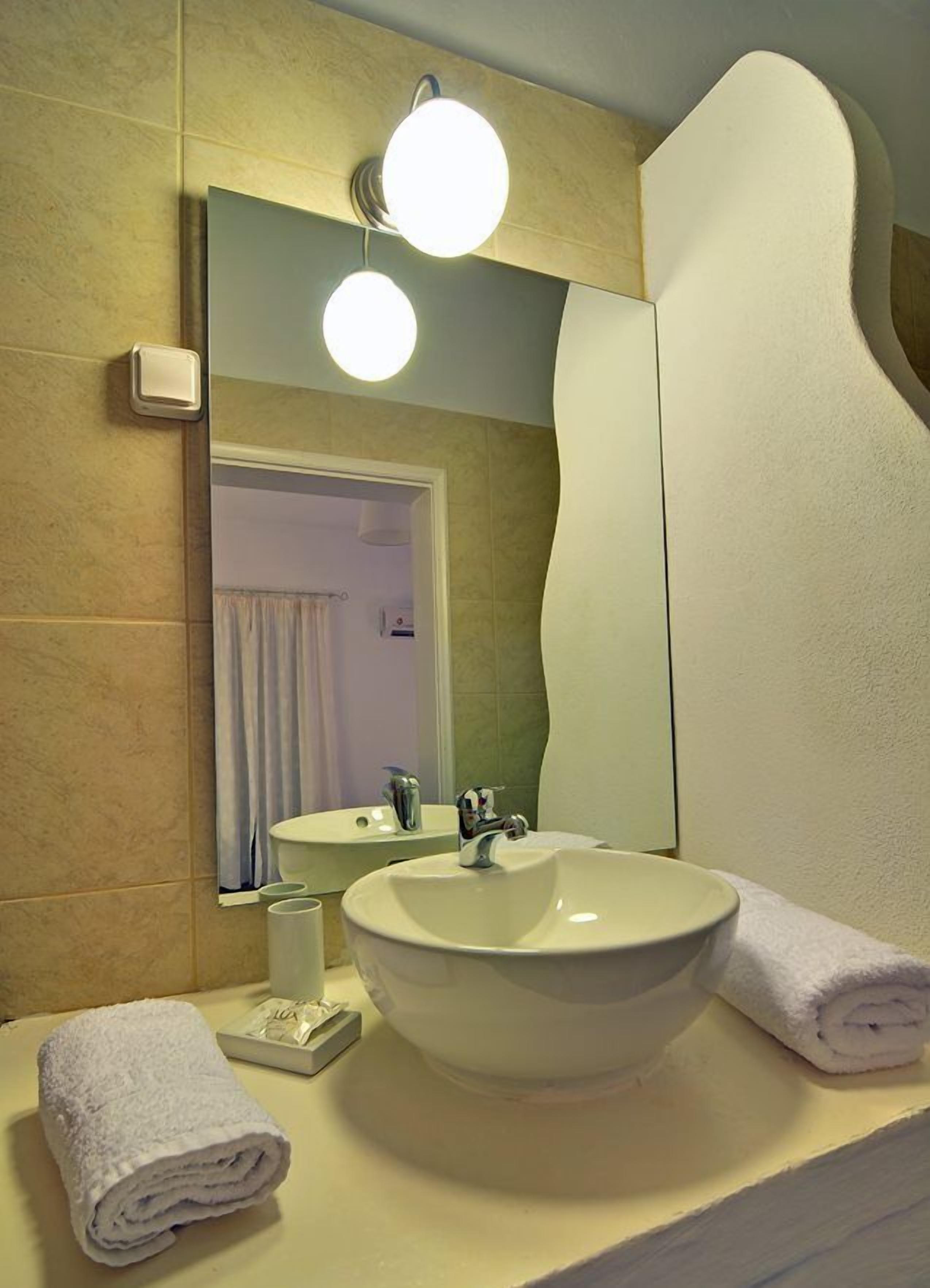 Un baño con un lavabo grande, dos luces redondas en la pared, un espejo y una toalla sobre el mostrador.