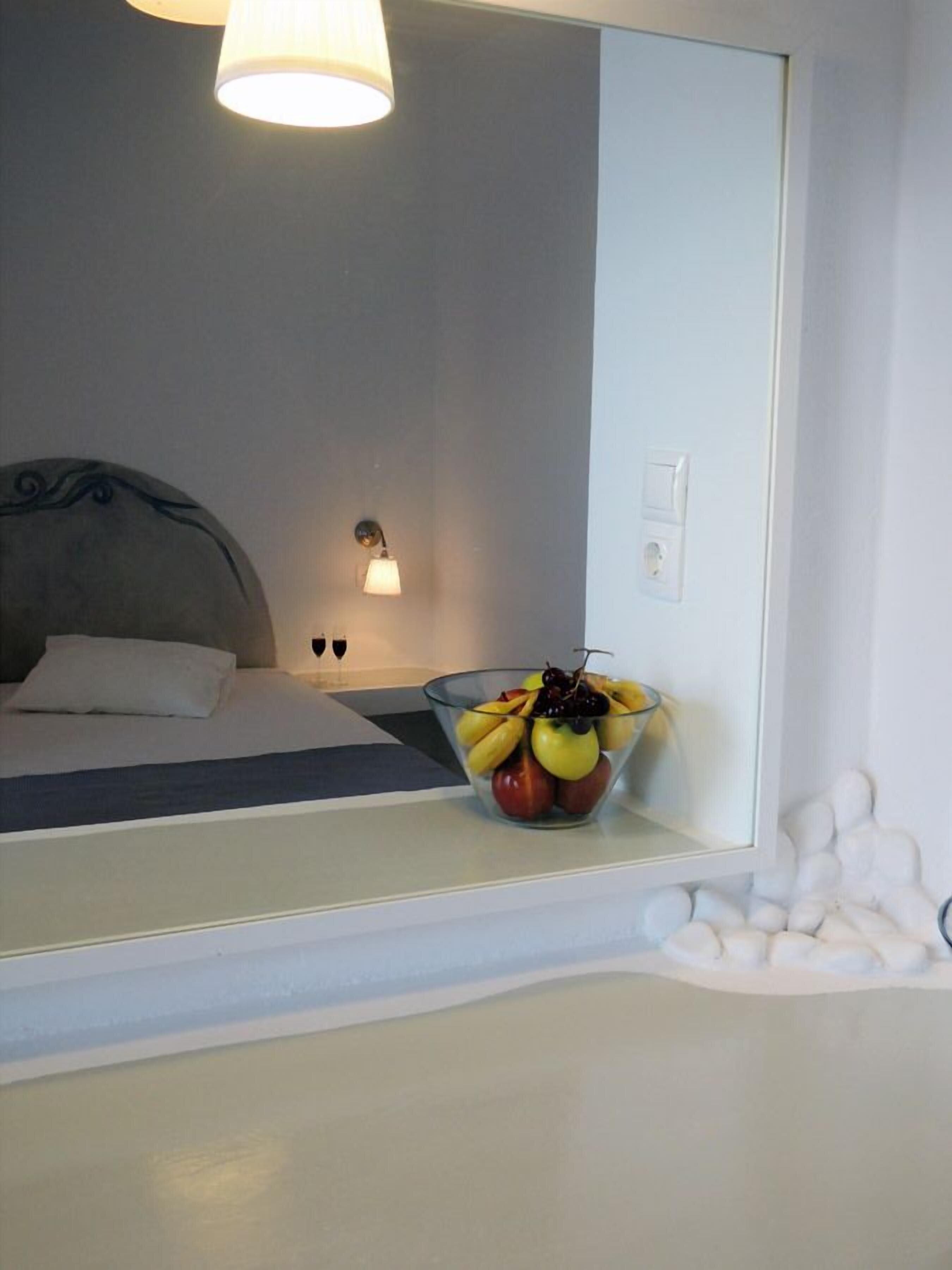 Habitación de hotel con una cama, una mesita de noche con frutero, una lámpara de pared y un espejo grande que refleja la habitación.