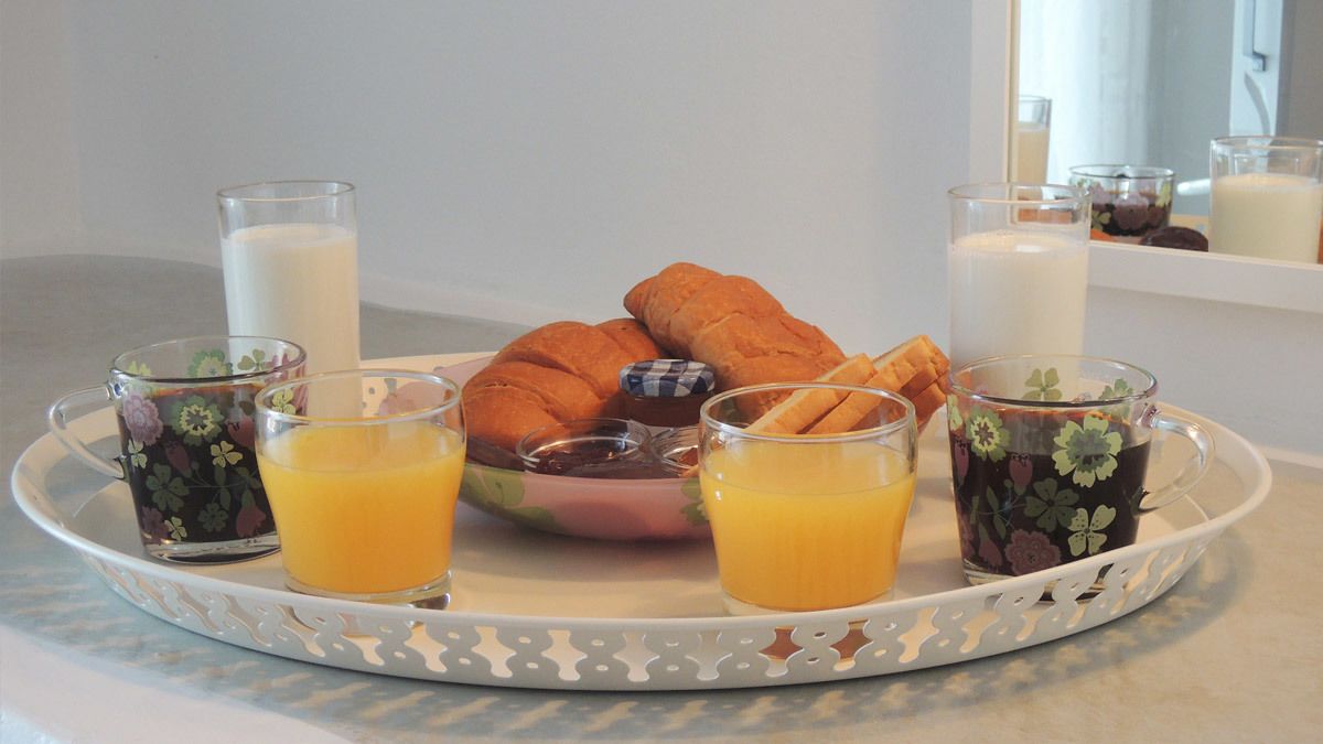 A breakfast tray with croissants, orange juice, milk, and jam.