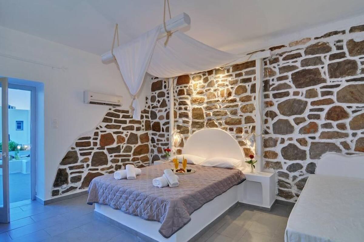 A bedroom with a stone wall, a bed with a white headboard, and a balcony.
