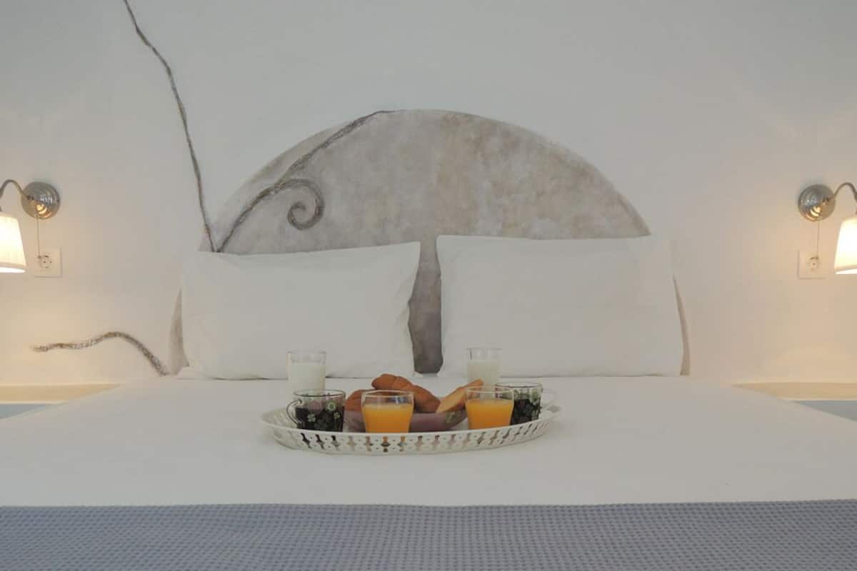 A bed with a white headboard, two wall-mounted lamps, and a tray with breakfast items.